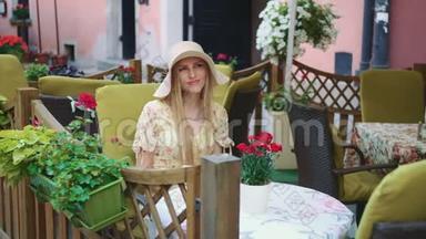 在外面餐馆里微笑的女人。 在舒适的街道上，坐在外面餐馆里的一位开朗的年轻女人。